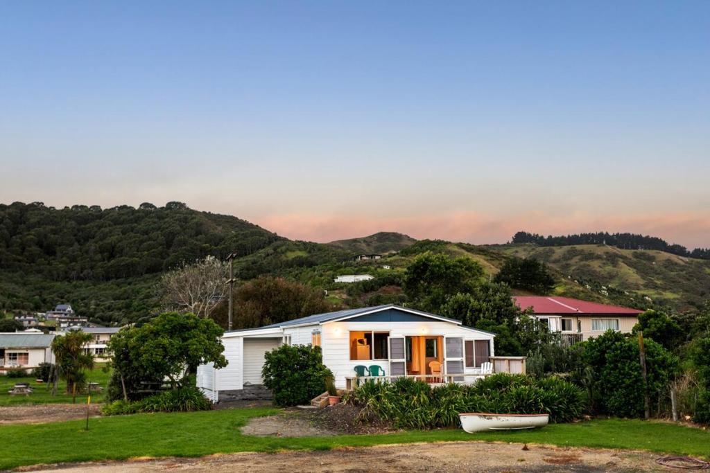 a white house with a boat in the yard at Coastal Comfort Holiday Home 100m to Mahia Beach in Mahia