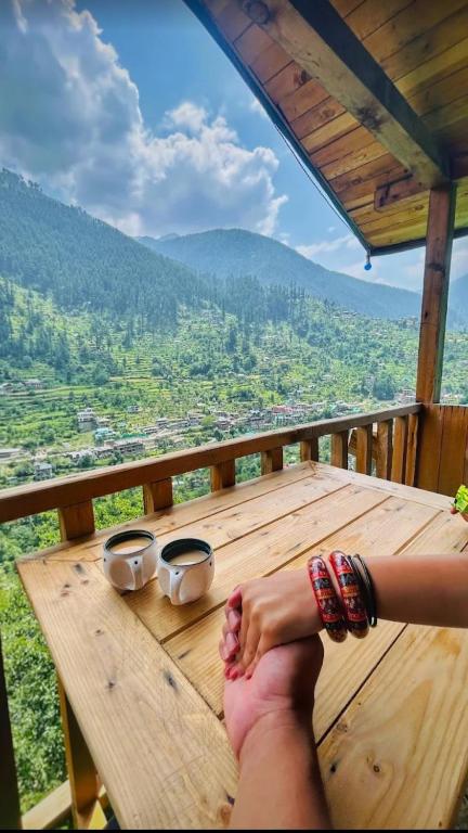 a person with their feet on a wooden table on a balcony at The Midhimalayan Jibhi in Jibhi