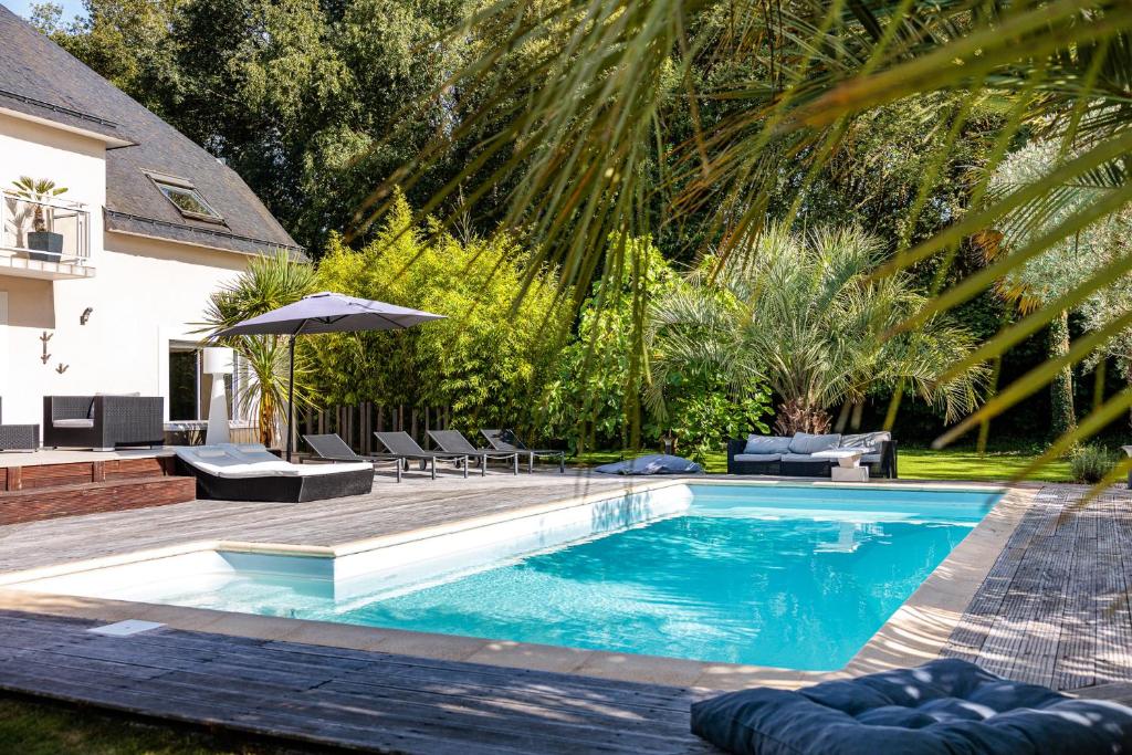 einen Pool mit Stühlen und einem Sonnenschirm neben einem Haus in der Unterkunft Villa Markaly in Vigneux-de-Bretagne