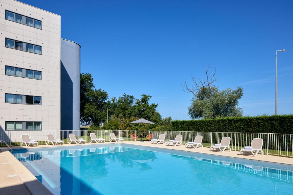 une piscine avec des chaises longues et un bâtiment dans l'établissement Zenitude Hôtel-Résidences Bordeaux Aéroport Mérignac, à Mérignac