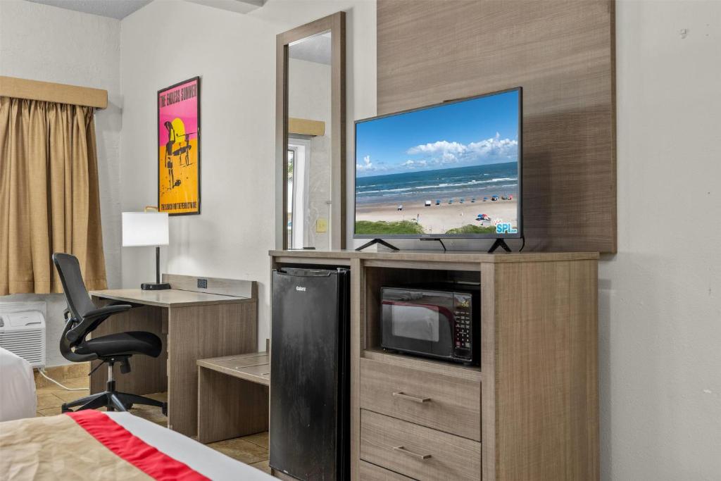 ein Hotelzimmer mit einem TV, einem Schreibtisch und einem Bett in der Unterkunft Ramada by Wyndham &amp; Suites South Padre Island in South Padre Island