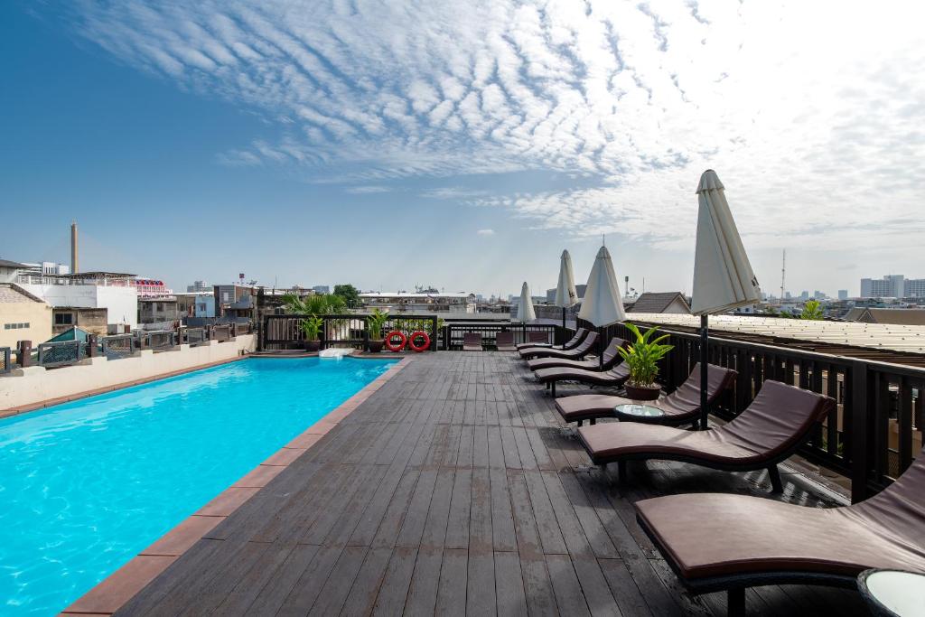 A rooftop pool deck with loungers, umbrellas and a city view.