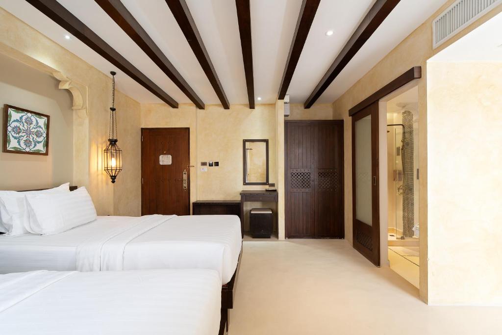 A bright twin room with two white beds, exposed ceiling beams and an en-suite bathroom doorway.