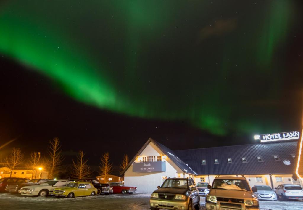 eine Gruppe von Autos, die vor einem Gebäude unter der Aurora geparkt werden in der Unterkunft Hotel Laxnes in Mosfellsbær
