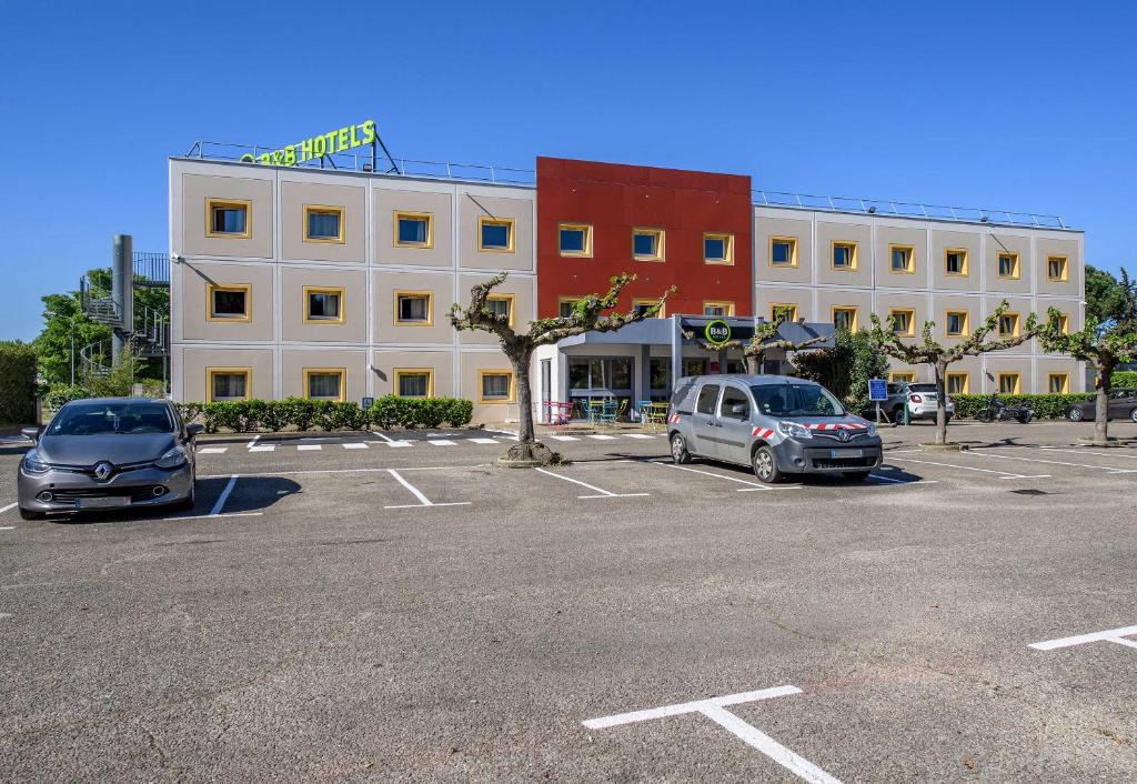 2 voitures garées sur un parking en face d'un immeuble dans l'établissement B&B HOTEL Nîmes Caissargues, à Caissargues