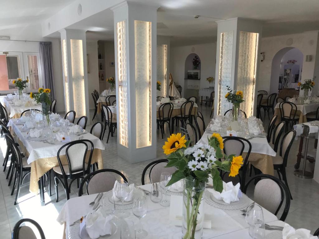 a dining room with white tables and chairs with flowers at Hotel Ristorante Borgo La Tana in Maratea