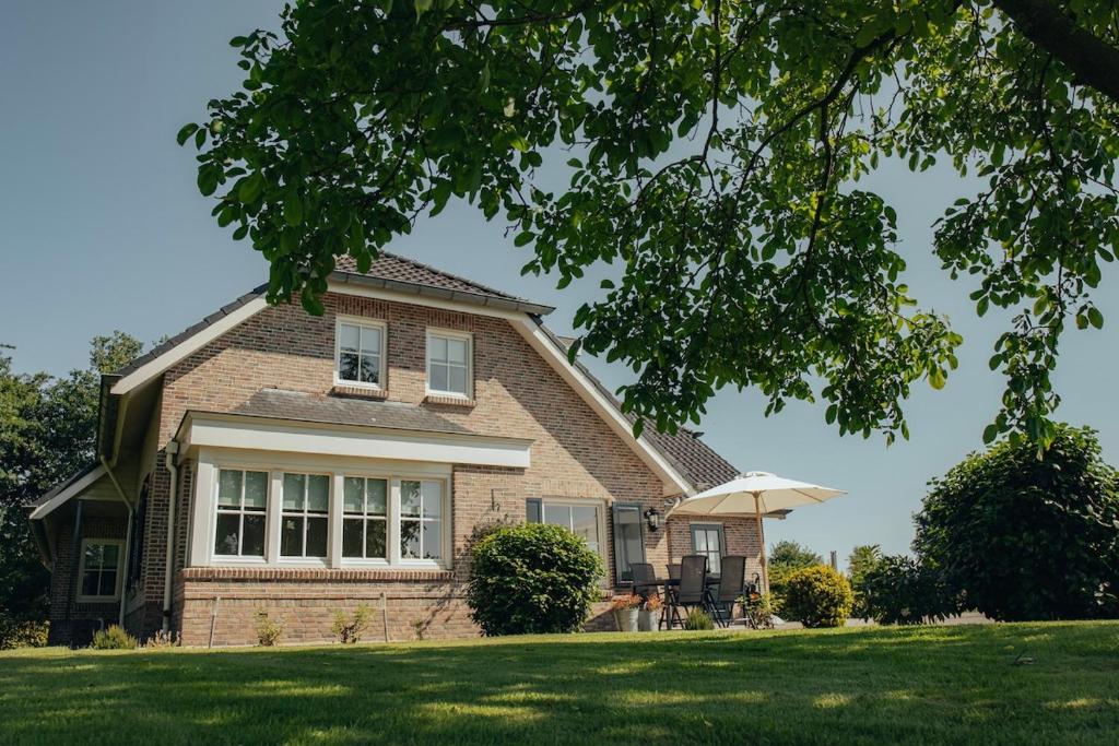 Una casa de ladrillo con una sombrilla en el césped. en NIEUW vanaf juli 2025 Vakantiewoning Borkeldrust, en Rijssen