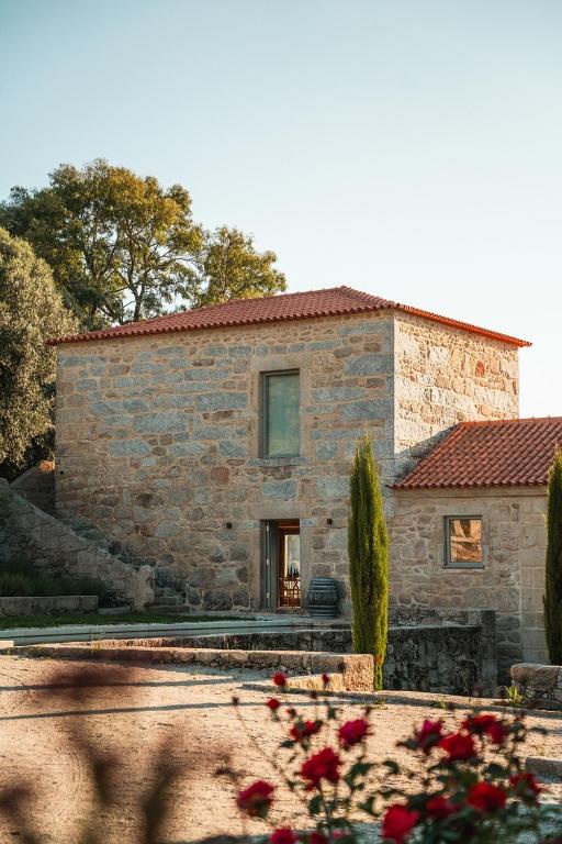 a stone house with red flowers in front of it at Quinta da Torre - Anselmo Mendes in Cortinhas