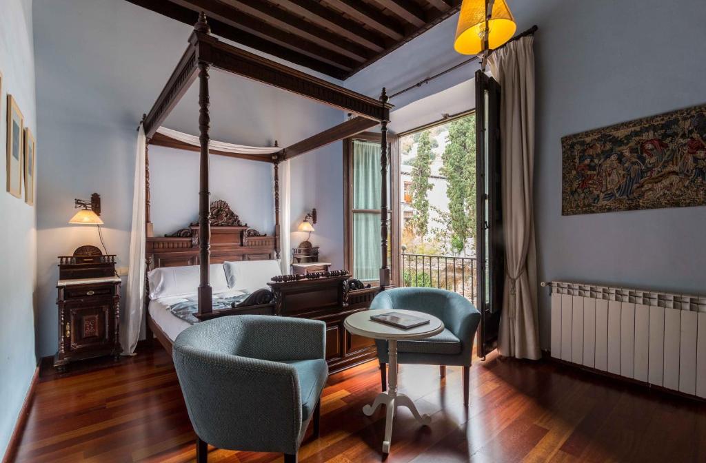 a bedroom with a canopy bed and two chairs at Palacio de Mariana Pineda in Granada