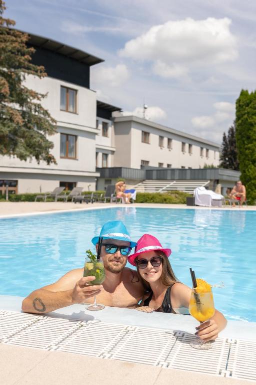 a man and a woman holding drinks in a swimming pool at Hotel Atlantis in Brno