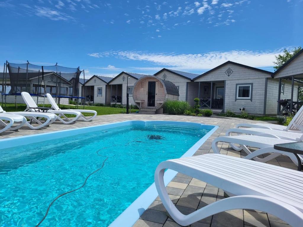 a swimming pool with white chairs and a white bench at Family Resort Gąski in Gąski