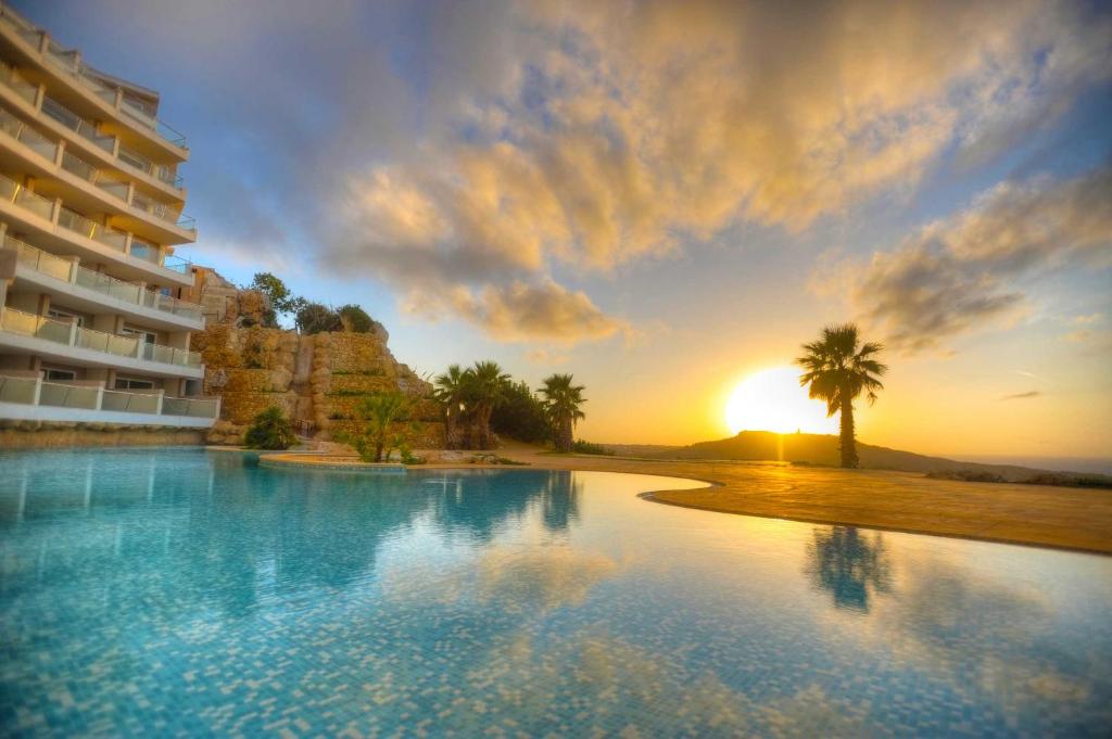 a view of a pool at a resort at sunset at Hal Saghtrija E7 in Żebbuġ