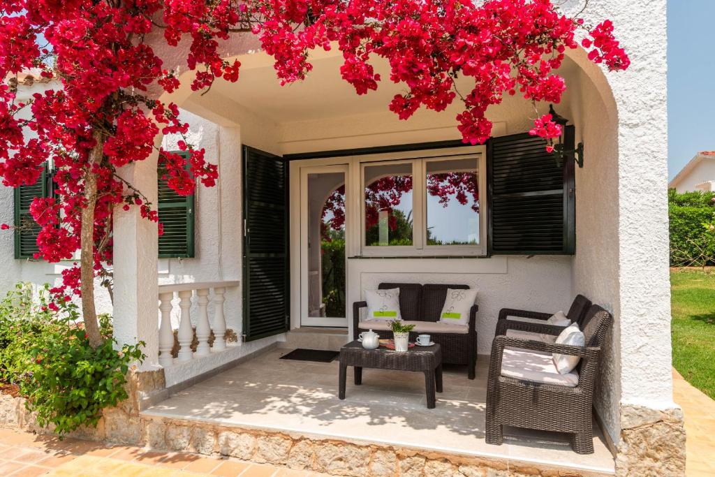 una casa con flores rojas en el porche delantero en Villa Juana - Torre Solí, en Son Bou