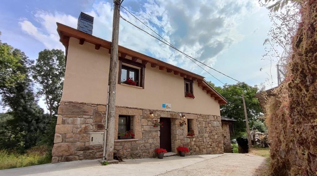 a small stone building with red flowers in front of it at Vivienda de Uso Turístico Los Castaños in San Román de Sanabria