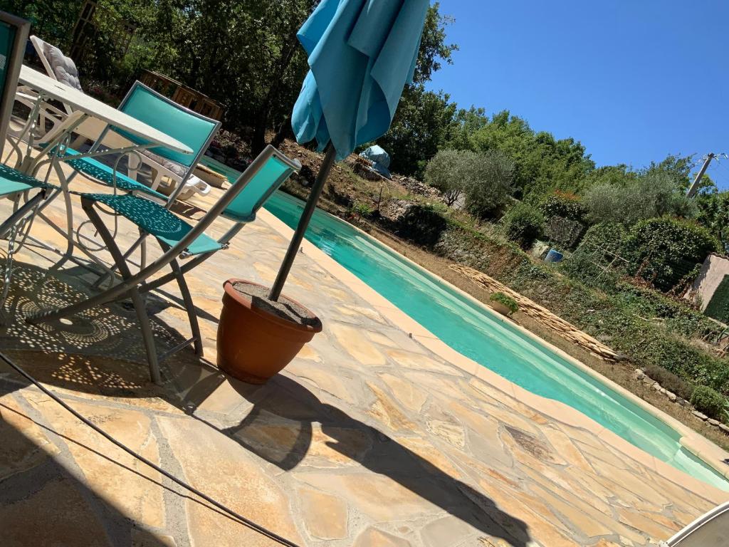 an umbrella and two chairs next to a swimming pool at Villa provençale La Banisté in Saint-Cézaire-sur-Siagne