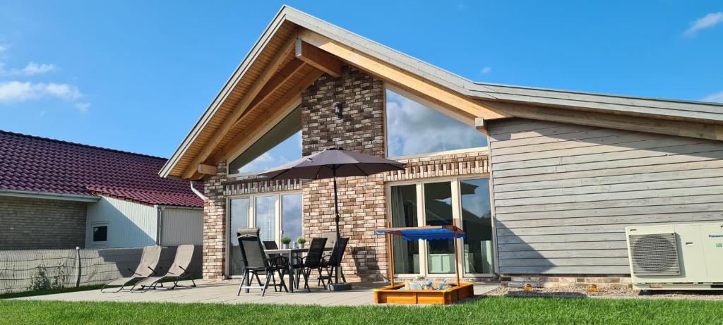 a house with chairs and an umbrella on a patio at Haus WattErlebnis - Urlaub mit Hund an der Nordseeküste in Sehestedt