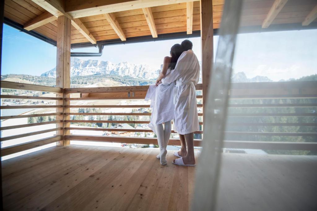 Una coppia in piedi in una stanza che guarda fuori da una finestra di Hotel Ciasa Soleil a La Villa