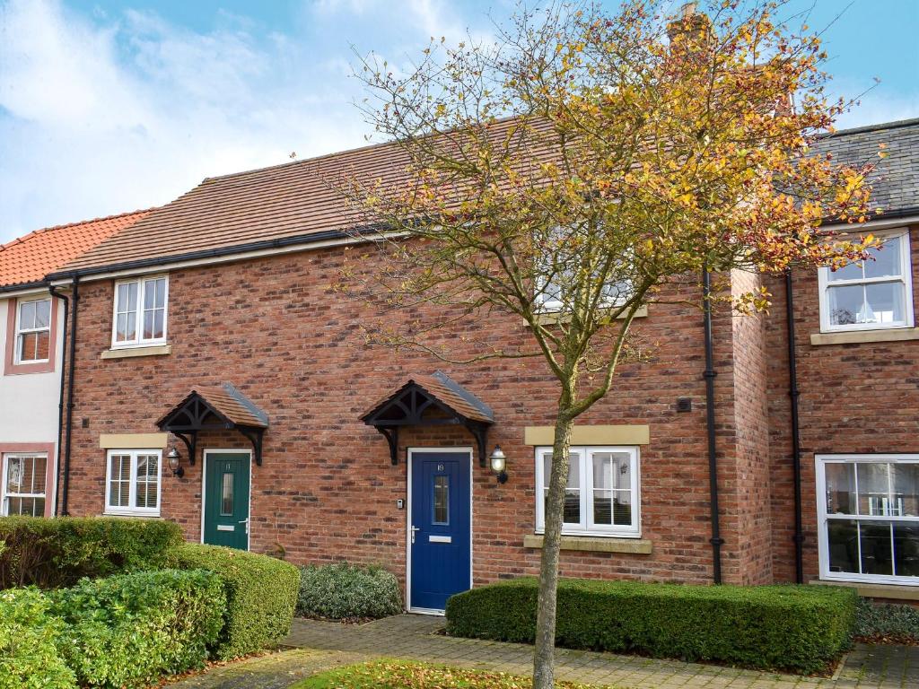 a brick house with a blue door and a tree at Perran Cottage in Reighton