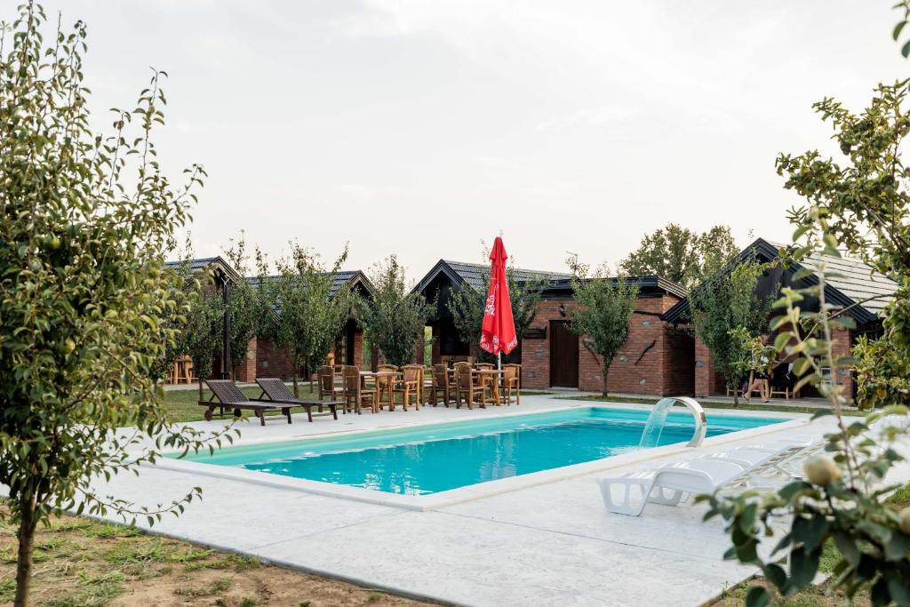 a swimming pool with chairs and a red umbrella at Etno Camp Lucić in Odžak