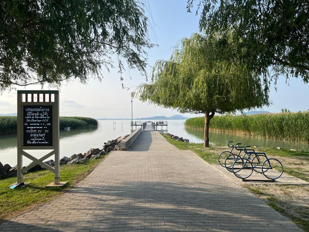 a bike path next to a lake with a sign at Hibiscus Apartman in Balatonfenyves