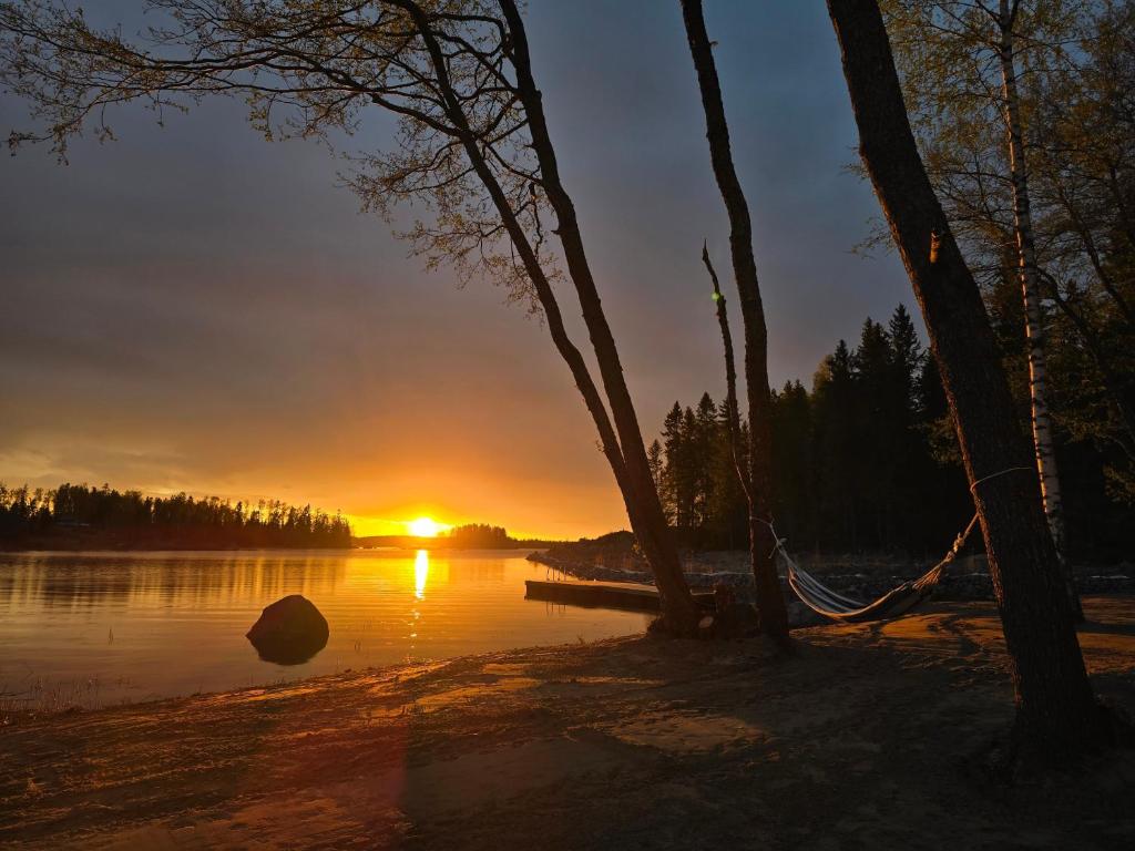 a sunset over a lake with a hammock at Stuga med strandbastu in Oravais