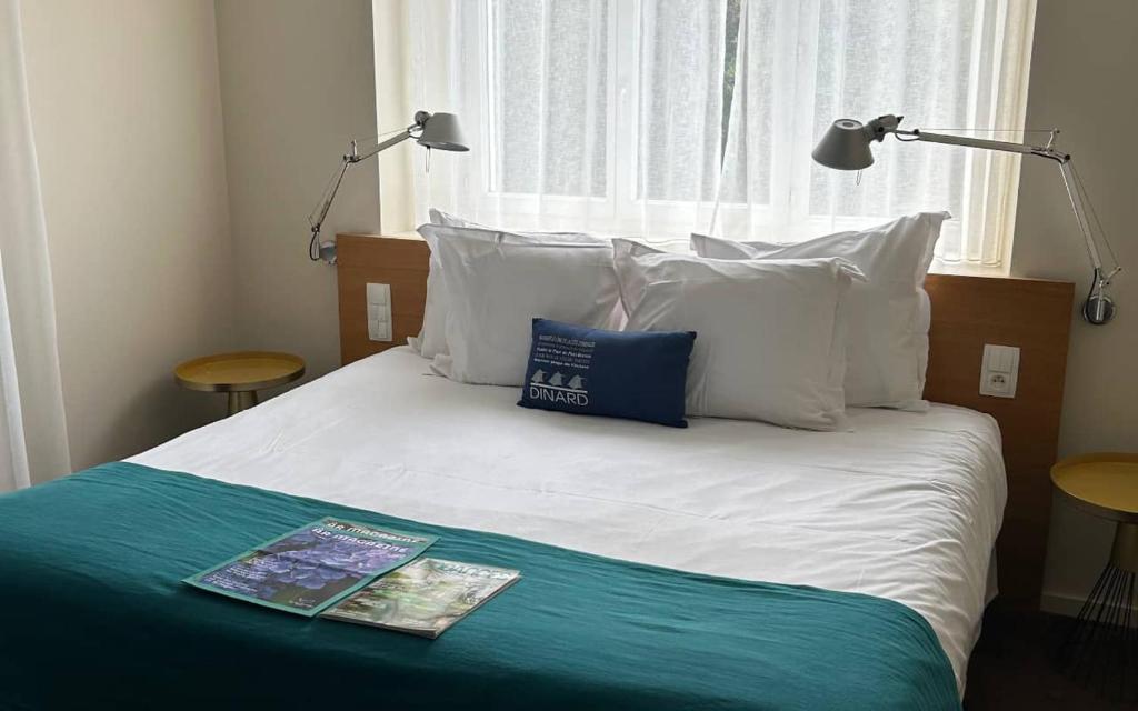 a bed with white pillows and a magazine on it at Hôtel De La Vallée in Dinard