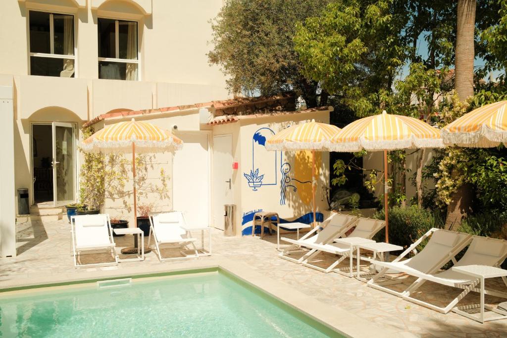 a swimming pool with lawn chairs and umbrellas at Hôtel Le Sud in Juan-les-Pins