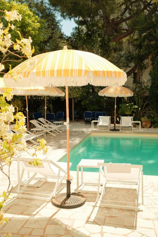 an umbrella and chairs next to a swimming pool at Hôtel Le Sud in Juan-les-Pins