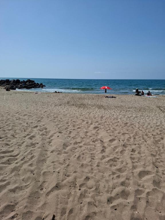 a sandy beach with a red umbrella and the ocean at Côté plage in Vias