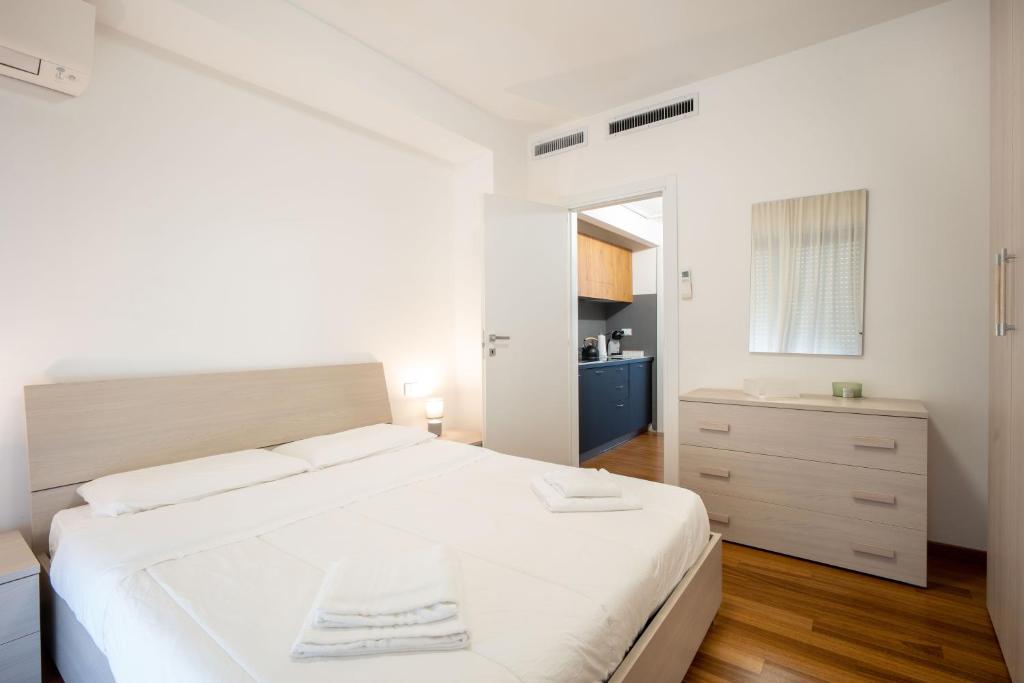 a white bedroom with a large bed and a kitchen at L'Alicanto - Bilocale zona centro in Pordenone