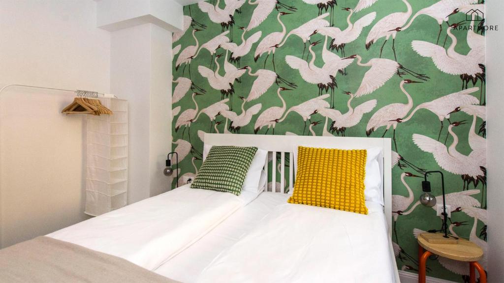 White twin beds against green crane wallpaper, yellow and green pillows, open clothes rack