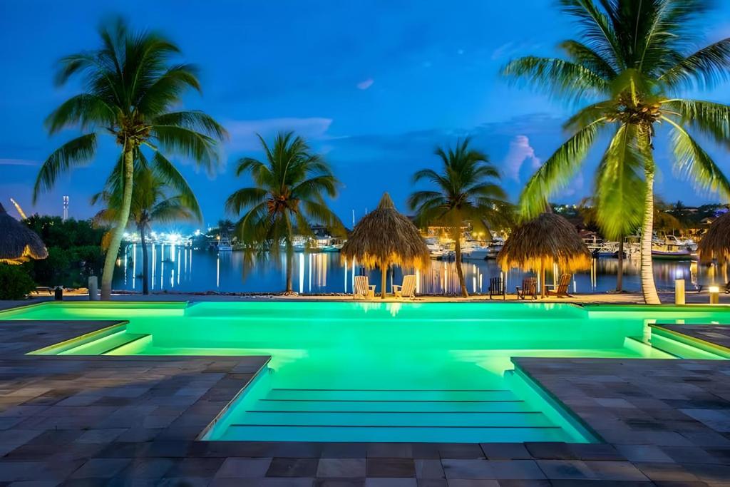 una piscina con palmeras y el océano por la noche en Luxury 4 Bedroom apartment, Pool, Private beach, Jan Thiel, en Willemstad