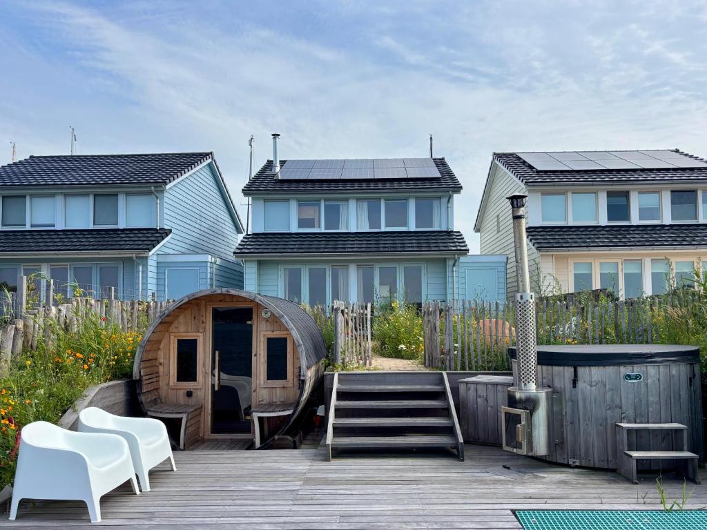 una terraza de madera con sillas blancas y una casa en Luxe woning met hottub en zeezicht VP074, en Wieringerwerf
