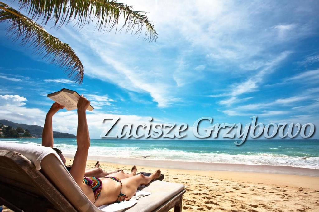 a woman laying on a beach reading a book at Zacisze Grzybowo in Grzybowo