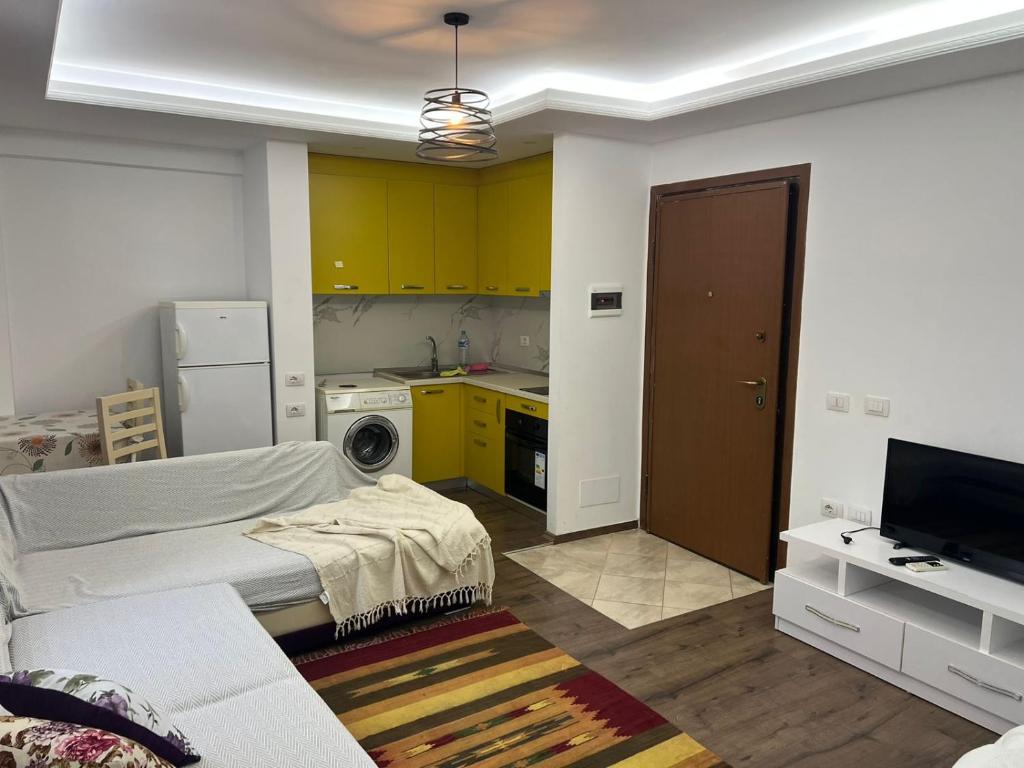 a living room with a bed and a kitchen with yellow cabinets at Brecani apartament 2 in Lezhë