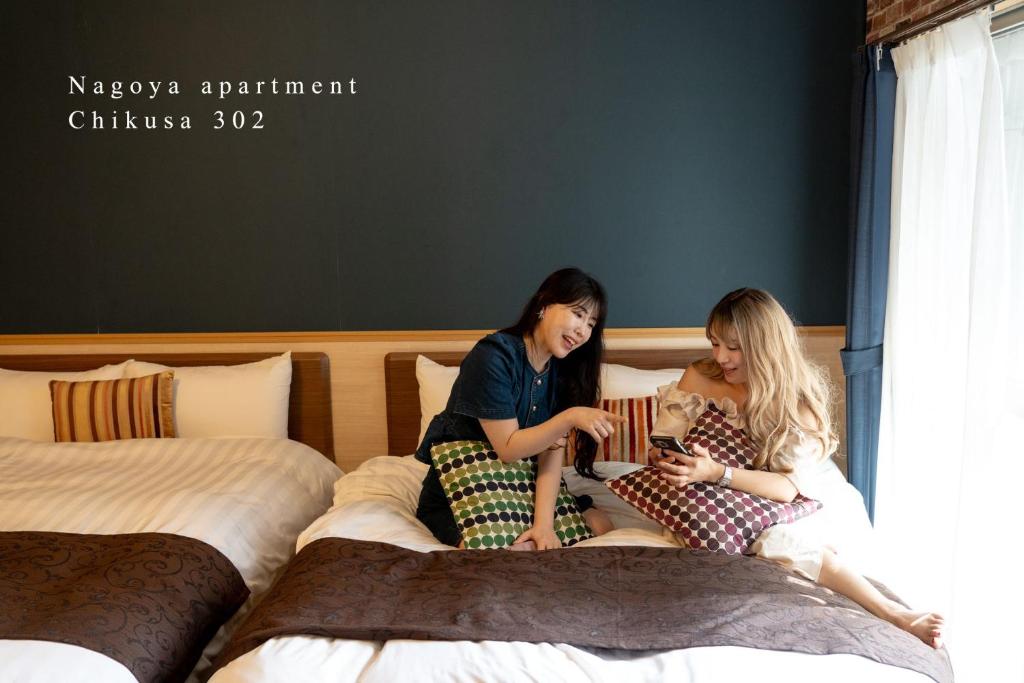 zwei Mädchen, die auf Betten sitzen und ihre Handys ansehen in der Unterkunft Prosper 5th bldg 302 in Nagoya