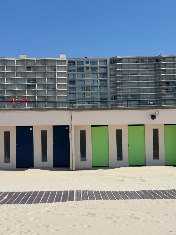 un bâtiment avec des portes vertes devant un grand immeuble dans l'établissement LTPP T2 face mer, à Le Touquet-Paris-Plage