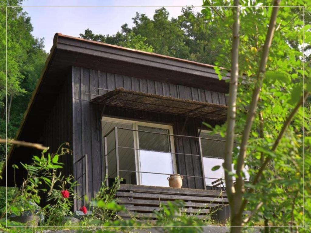 a small black cabin with a window in the woods at La Pause En Soi - Cabanes climatisées avec Jaccuzi privatif en option in Ponlat-Taillebourg