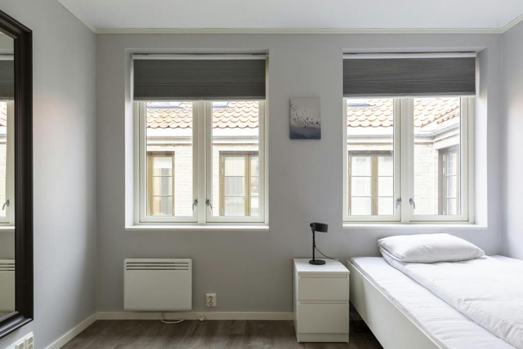 a white bedroom with two windows and a bed at Central and Spacious Apartment for 6 in Trondheim