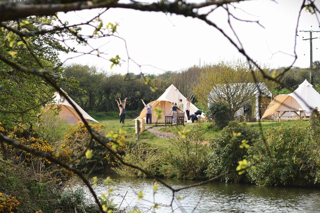 a group of tents in a field next to a river at Mallard - 5m Luxury Bell Tent at Tregonetha Lake - Tylda Tents in Saint Columb Major