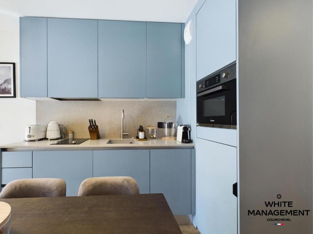 une cuisine avec des placards bleus et une table avec des chaises dans l'établissement Résidence Ariondaz Hellebore - Beau T2 Cabine pour 5 personnes MAE-7724, à Courchevel