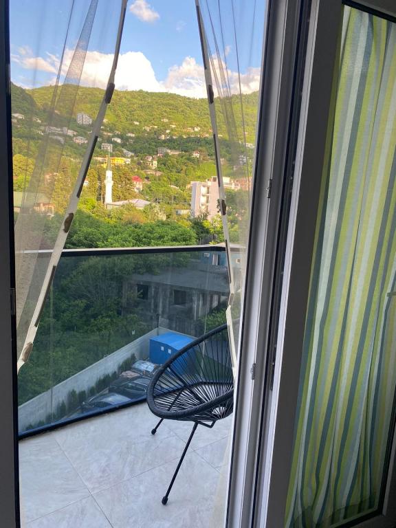 une chaise assise sur un balcon regardant par une fenêtre dans l'établissement Сдается двухкомнатная квартира с балконом в Гонио с прекрасным видом на горы, à Itʼkhvisi