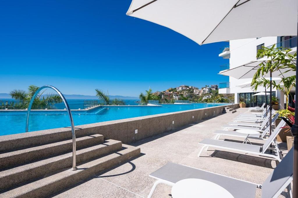 a row of white lounge chairs next to a swimming pool at Zantamar PH608B, frente al mar in Cruz de Huanacaxtle