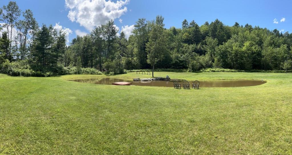 a green field with a pond in the middle at Sunny 2BR with Pond, Fireplace, Walk to Stowe in Stowe