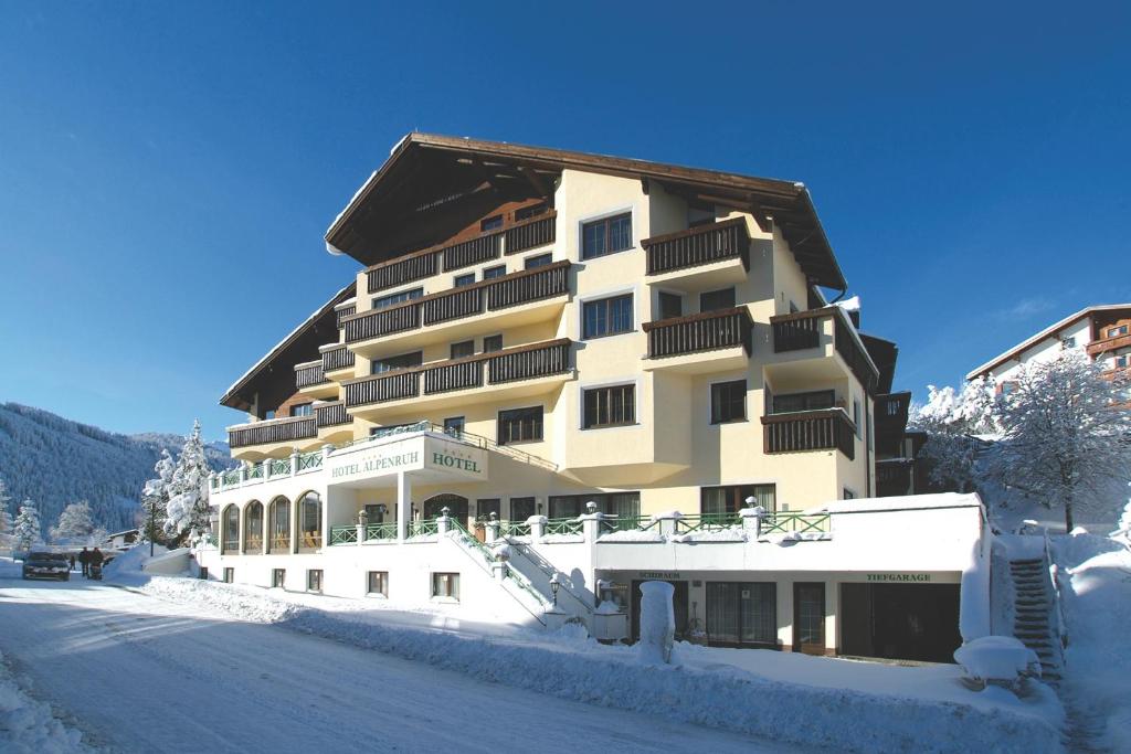 a large building in the snow with a road in front at Hotel Garni Alpenruh-Micheluzzi in Serfaus