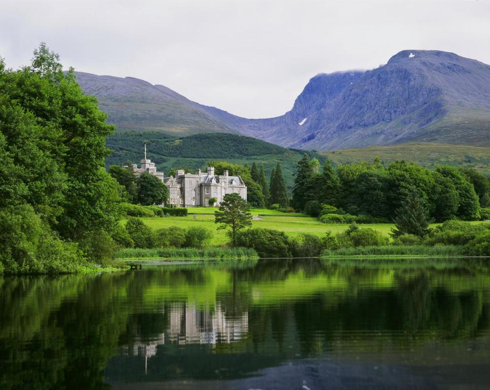 un château au bord d'un lac avec des montagnes en arrière-plan dans l'établissement Inverlochy Castle Hotel, à Fort William