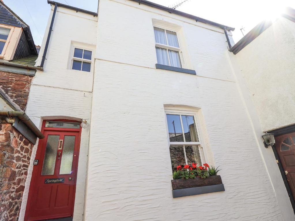 a white house with a red door and flowers in a window at Springfield in Kingsand