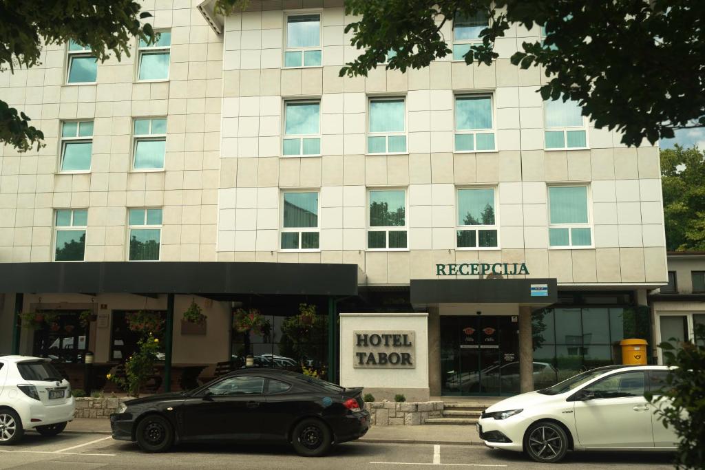 due auto parcheggiate di fronte a un edificio di Hotel Tabor a Sežana