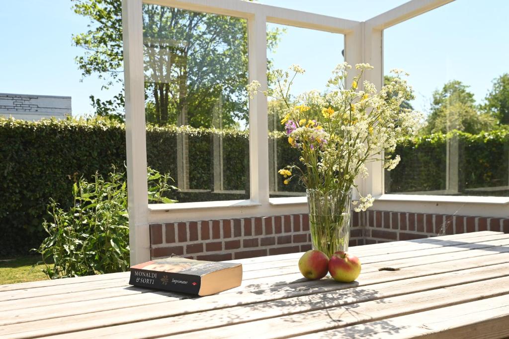 a table with apples and a vase of flowers and a book at Villa Mer - Terra Nova, detached bungalow with XXL garden, near the beach in Cadzand