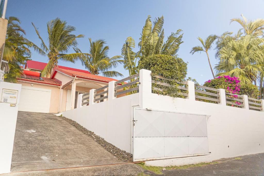une clôture blanche devant une maison plantée de palmiers dans l'établissement Villa Ile d'Eden - Vue mer-Piscine - By Sister Home, à Sainte-Marie
